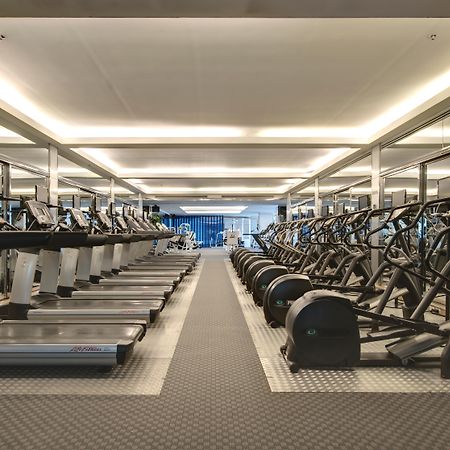 Pathumwan Princess Hotel - Sha Extra Plus Certified Banguecoque Exterior foto The photo shows a modern gym space featuring rows of exercise equipment. On one side, there are several treadmills and possibly elliptical machines lined up. The other side has stationary bikes and strength training equipment, arranged neatly. The gy