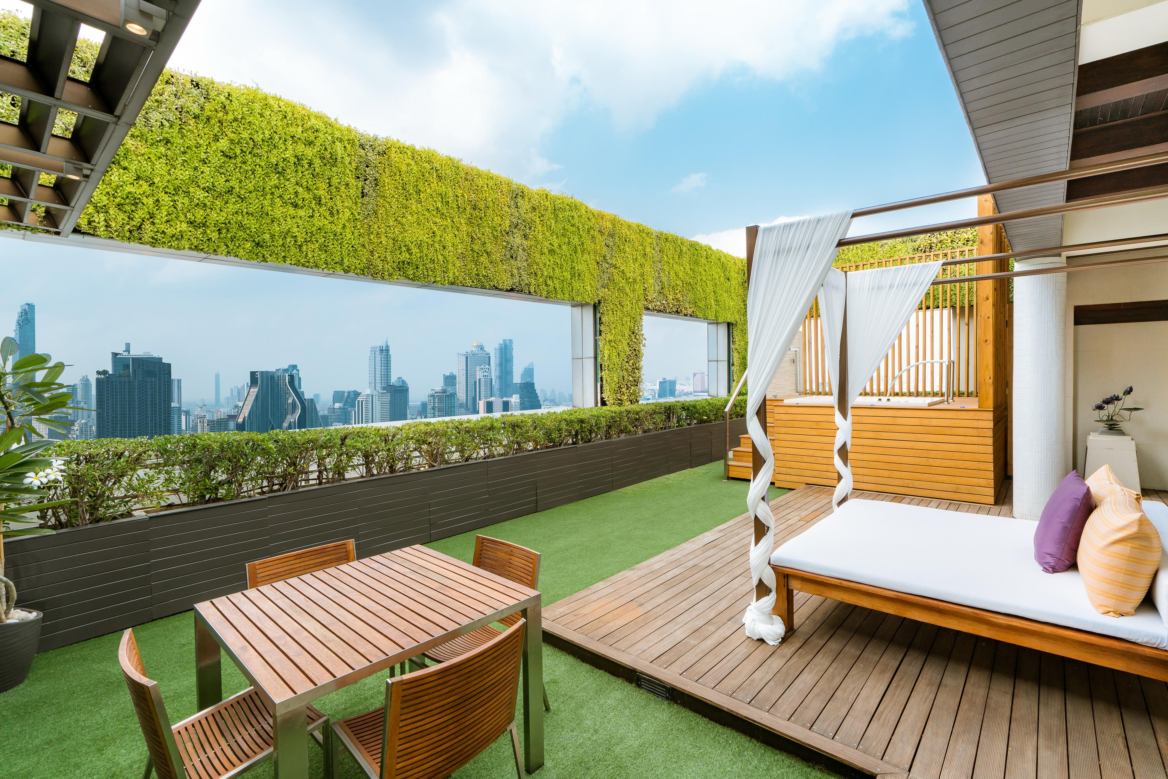 Pathumwan Princess Hotel - Sha Extra Plus Certified Banguecoque Exterior foto The image shows a beautiful rooftop terrace featuring a stunning city view. The space is adorned with a green wall or hedge, providing a lush backdrop. There is a wooden table with several chairs, suggesting a perfect spot for dining or relaxation. N
