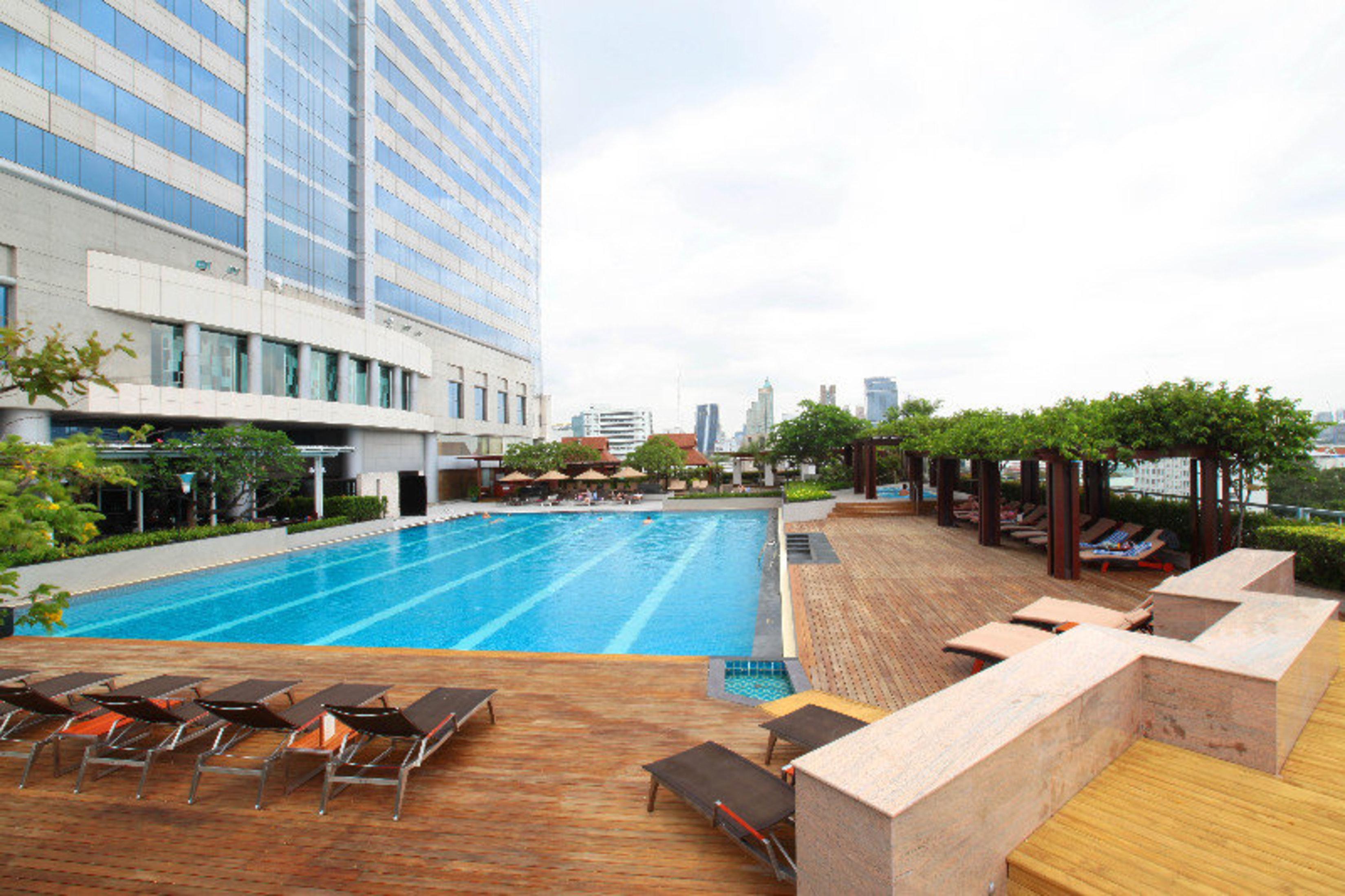 Pathumwan Princess Hotel - Sha Extra Plus Certified Banguecoque Exterior foto The photo depicts a modern swimming pool area located in an outdoor setting. The pool features clear blue water and is surrounded by wooden decking. There are several lounge chairs arranged around the pool, inviting for relaxation. In the background,