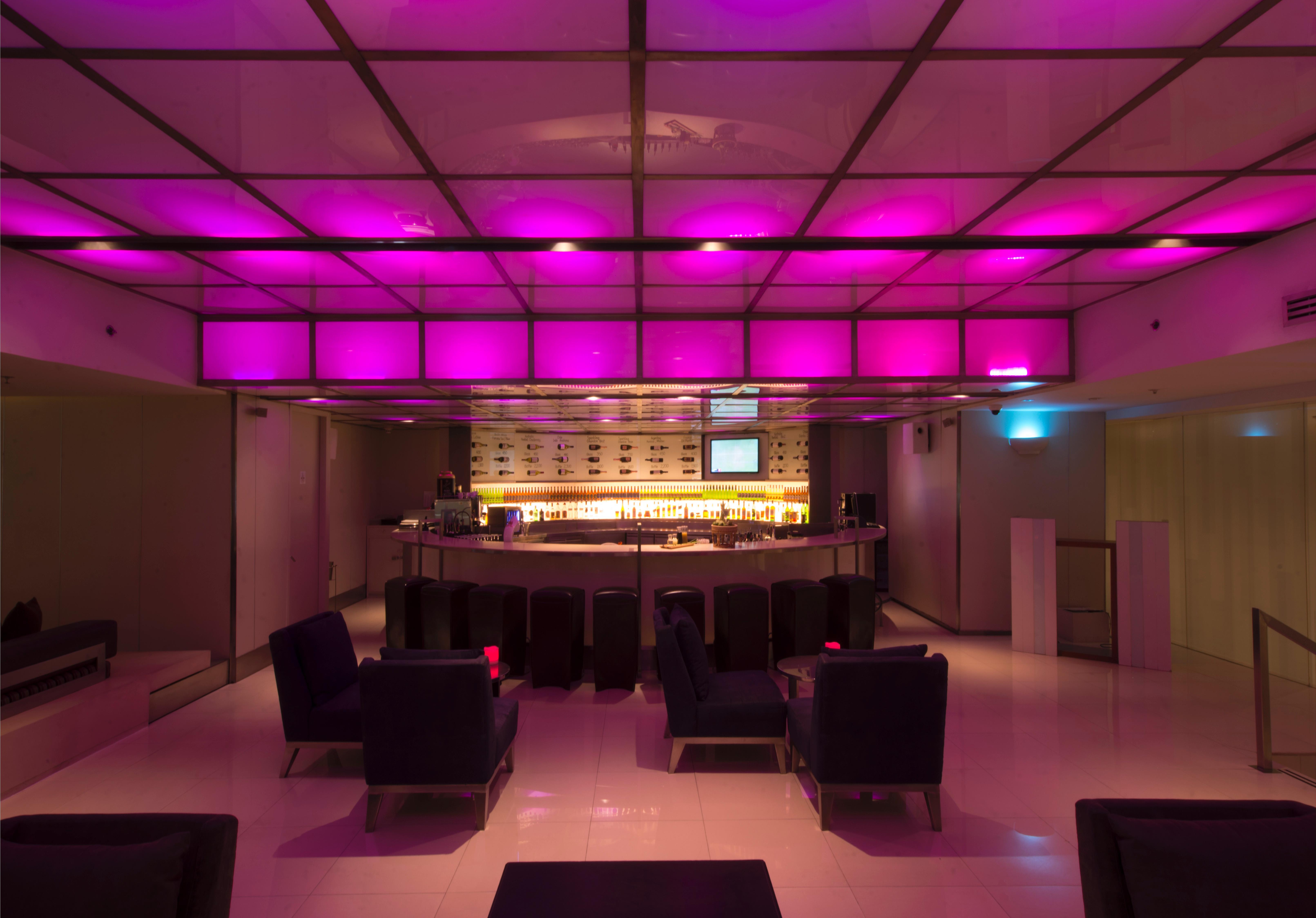 Pathumwan Princess Hotel - Sha Extra Plus Certified Banguecoque Exterior foto The photo shows a modern bar interior with a sleek design. The lighting features a pink hue that illuminates the ceiling, creating a vibrant atmosphere. In the center, there is a rounded bar counter with a well-stocked shelf behind it. The seating ar