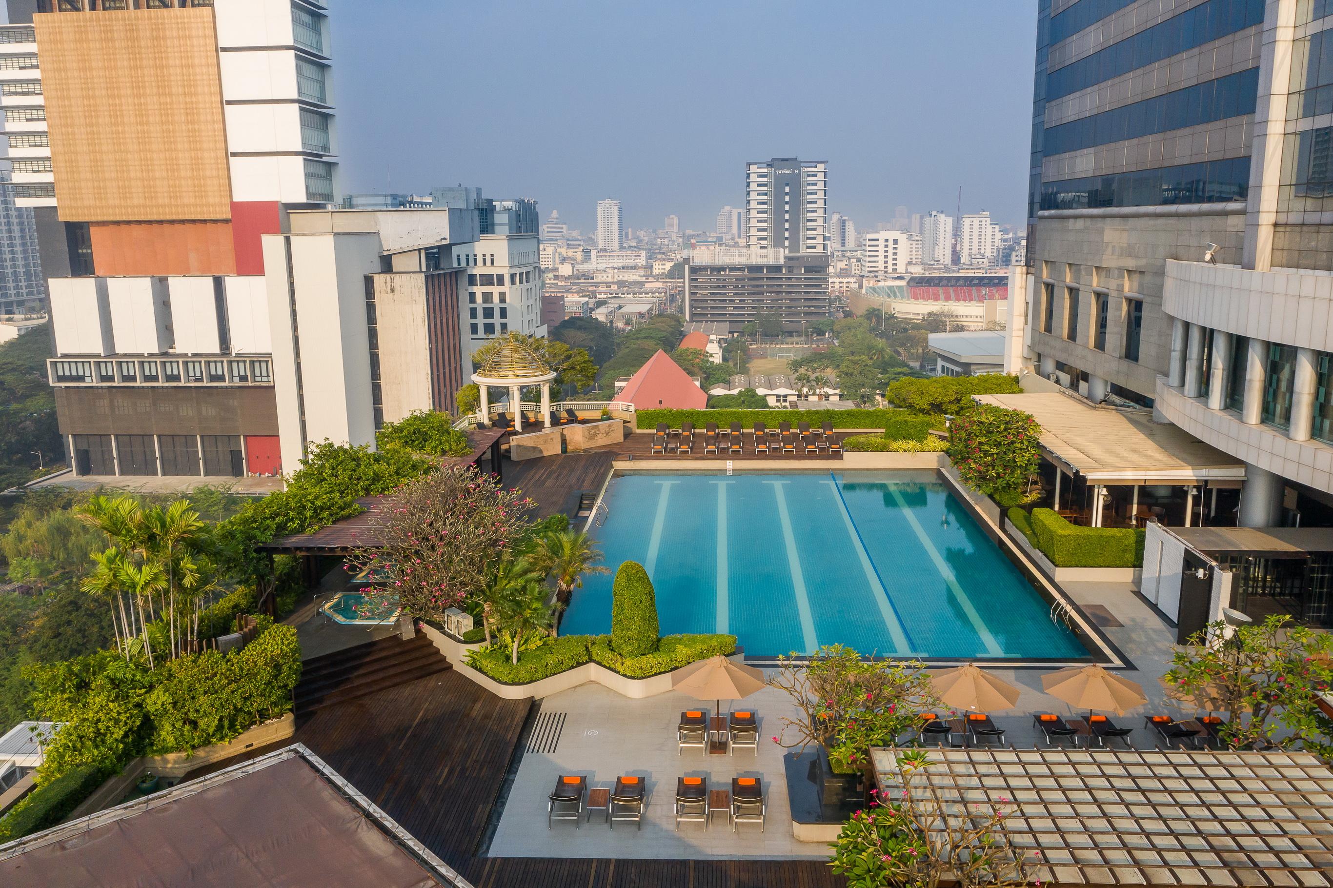 Pathumwan Princess Hotel - Sha Extra Plus Certified Banguecoque Exterior foto The photo shows a rooftop swimming pool surrounded by landscaped greenery and lounge chairs. The pool is large and rectangular, with clear blue water reflecting the sky. Around the pool, there are various seating areas with umbrellas, likely designed
