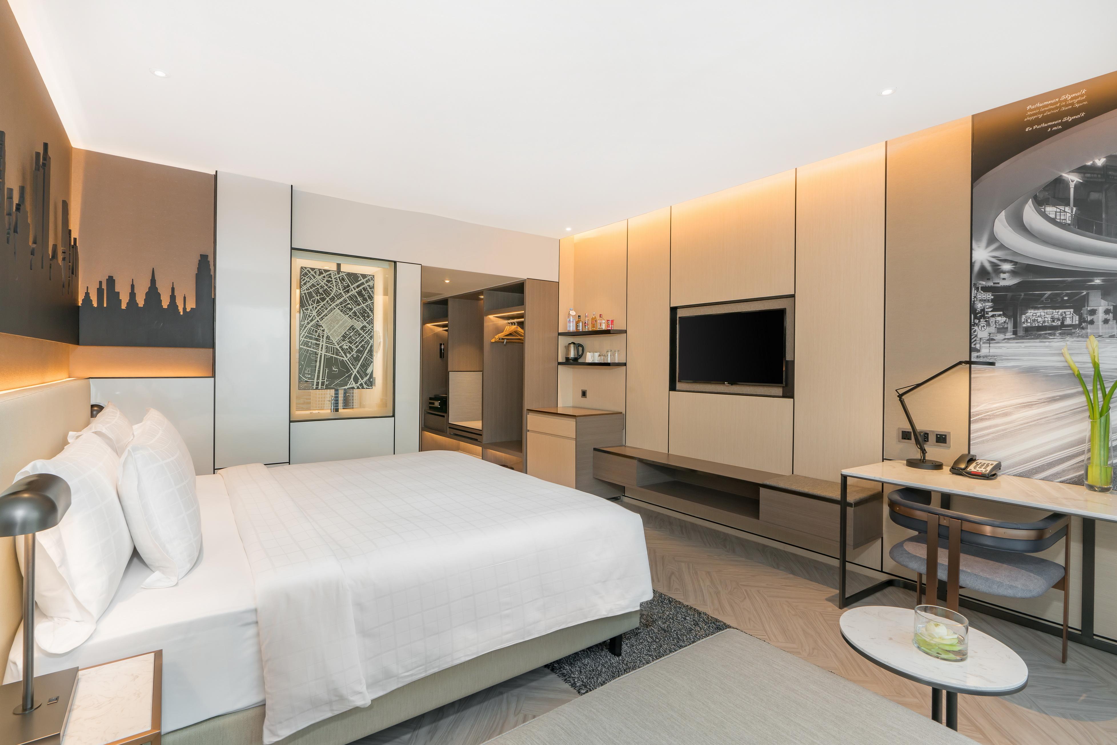Pathumwan Princess Hotel - Sha Extra Plus Certified Banguecoque Exterior foto The photo shows a modern hotel room with a contemporary design. It features a large bed with white linens and plush pillows. The room is well-lit with warm lighting, creating an inviting atmosphere. There is a wall-mounted flat-screen TV opposite the