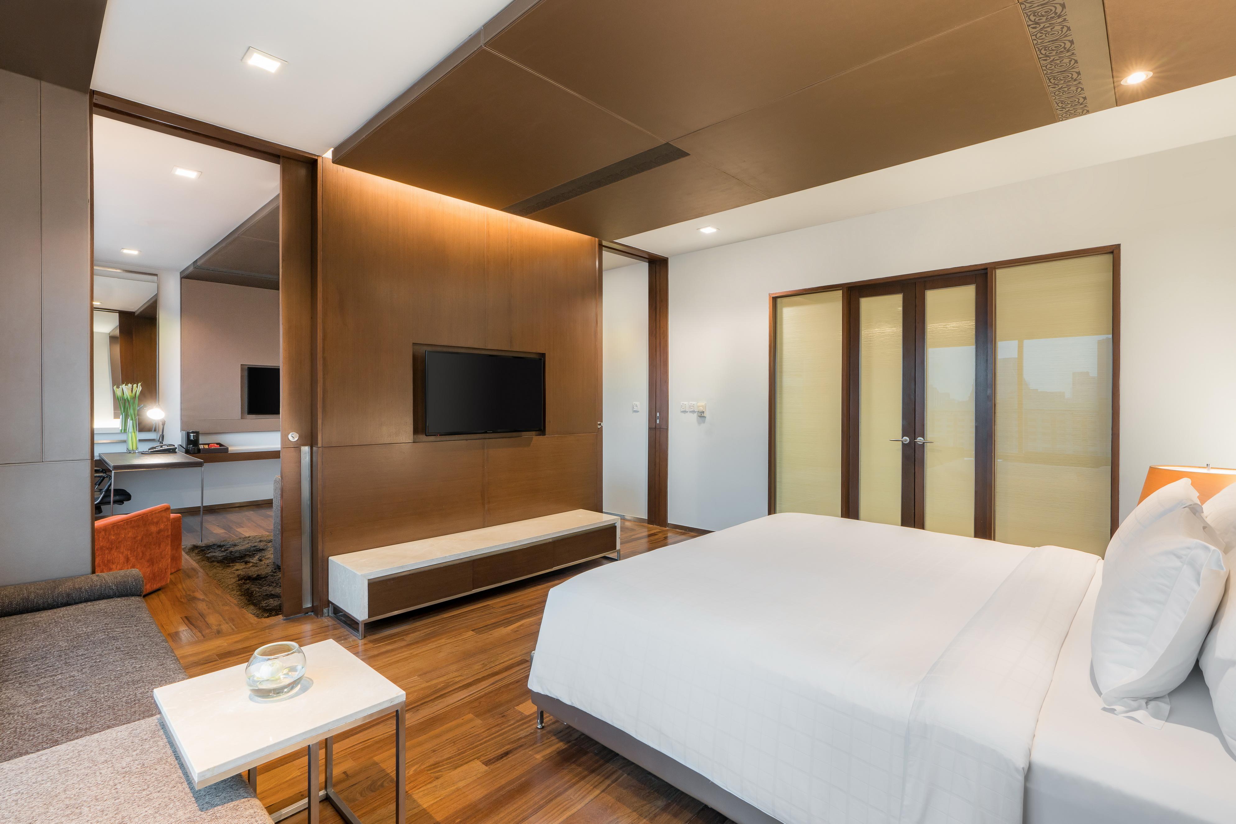 Pathumwan Princess Hotel - Sha Extra Plus Certified Banguecoque Exterior foto The photo shows a modern and stylish bedroom. It features a comfortable bed with white bedding, a sleek wooden floor, and a minimalistic design. There's a large television mounted on the wall opposite the bed. In the background, there are glass doors