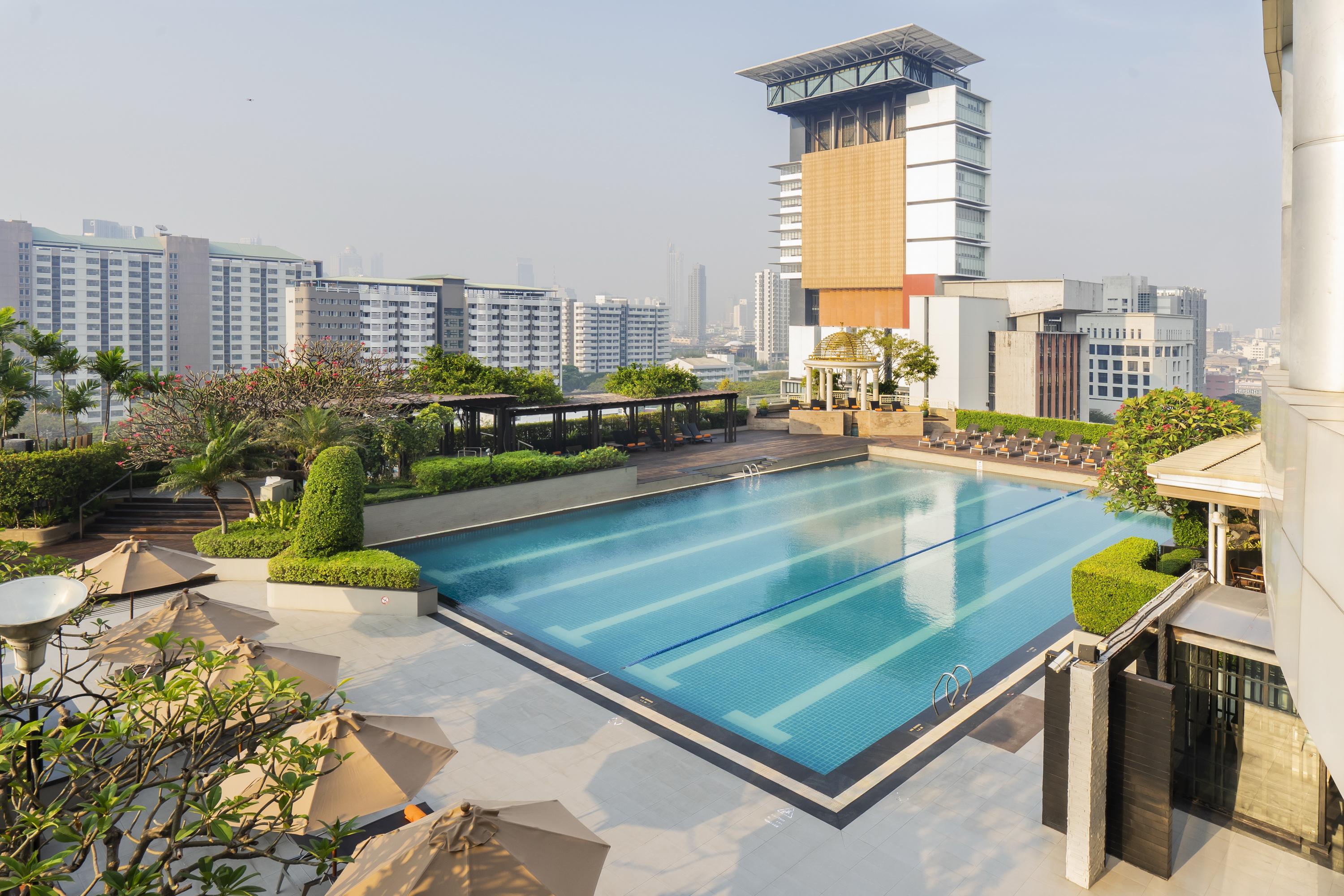 Pathumwan Princess Hotel - Sha Extra Plus Certified Banguecoque Exterior foto The photo shows a modern swimming pool area situated on a rooftop or an elevated location. The pool is large and rectangular, with clear blue water and several swim lanes marked. Surrounding the pool are well-maintained green lawns and neatly trimmed