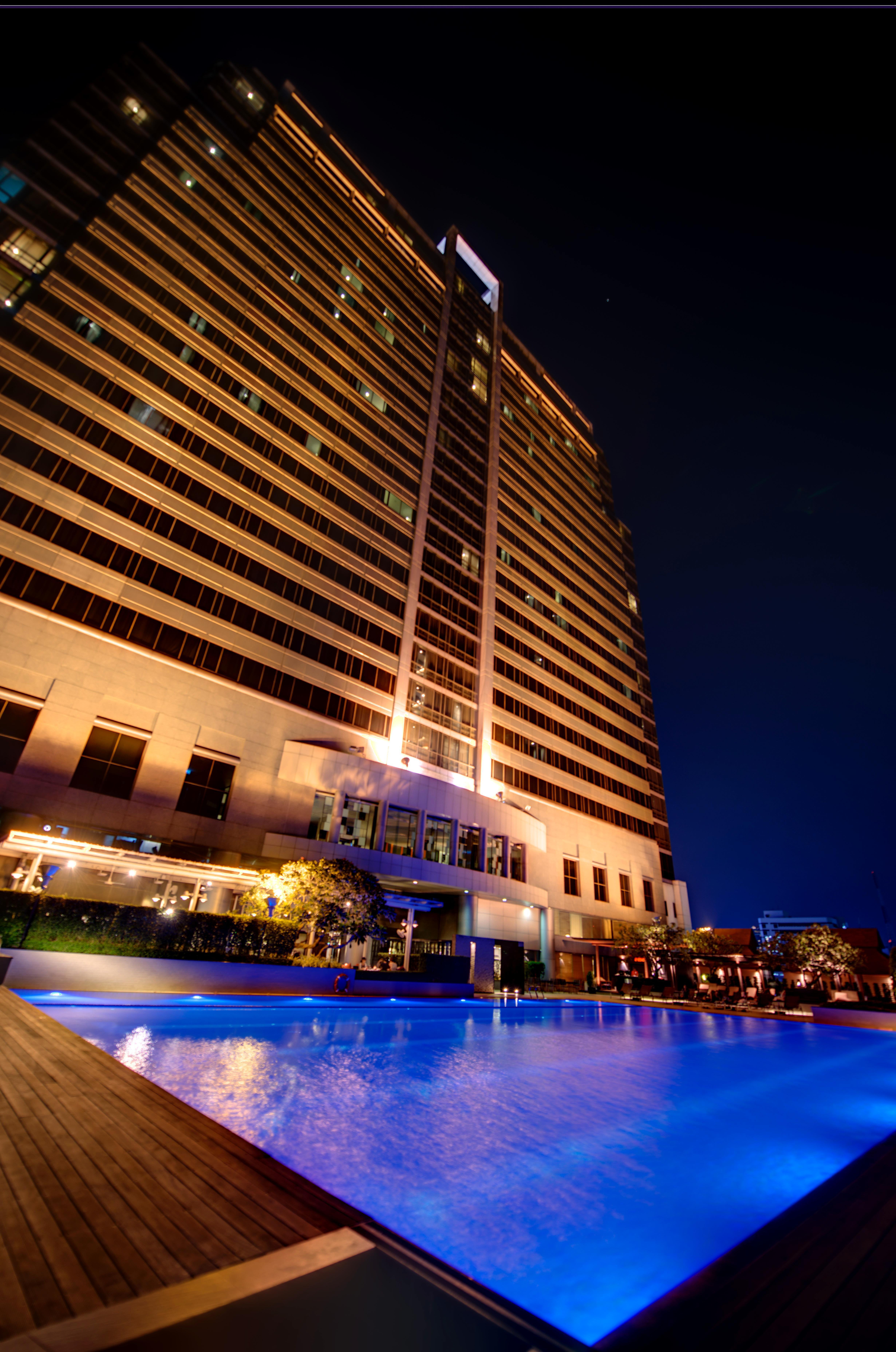 Pathumwan Princess Hotel - Sha Extra Plus Certified Banguecoque Exterior foto The photo shows a modern high-rise building illuminated at night. The structure features large windows and a sleek design, with warm lighting highlighting its facade. In the foreground, there appears to be a pool, reflecting the lights and adding to 