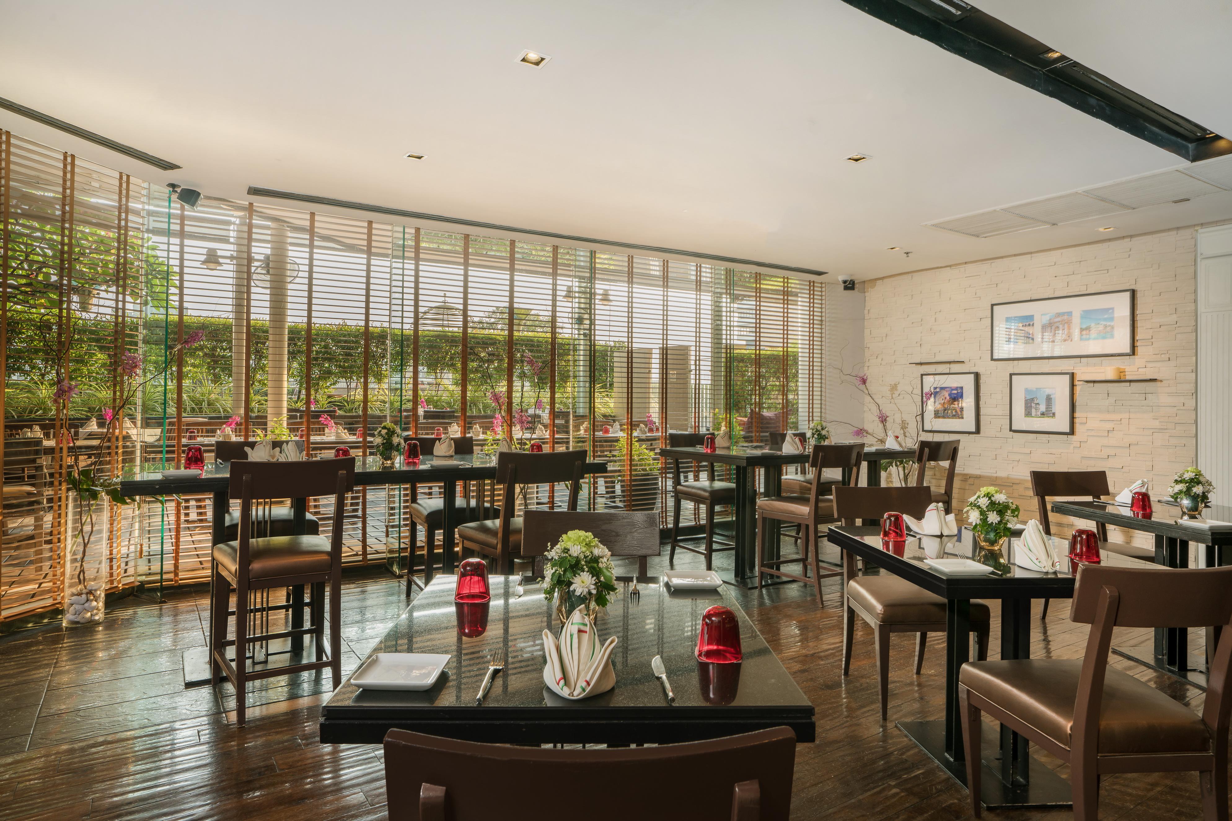 Pathumwan Princess Hotel - Sha Extra Plus Certified Banguecoque Exterior foto The photo shows an elegantly designed restaurant interior. It features dark wooden flooring and tables with neatly arranged place settings. Each table has a small centerpiece with flowers and red candles. Large windows with slatted blinds allow natur