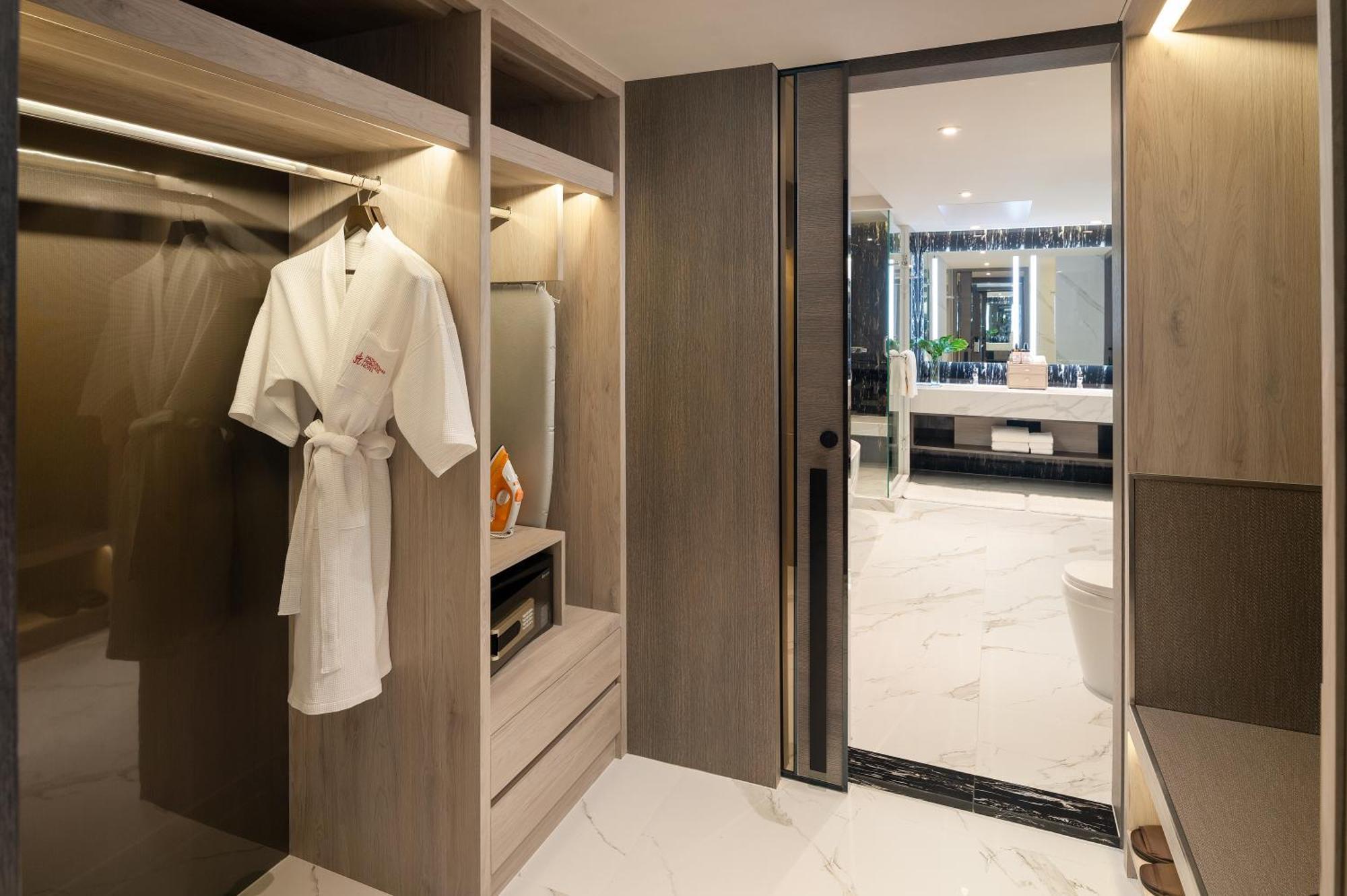 Pathumwan Princess Hotel - Sha Extra Plus Certified Banguecoque Exterior foto The photo shows a modern bathroom area featuring sleek wooden cabinetry and marble flooring. There is a white bathrobe hanging on a hanger within an open closet space. The design is minimalist, with clean lines and a contemporary aesthetic. To the ri