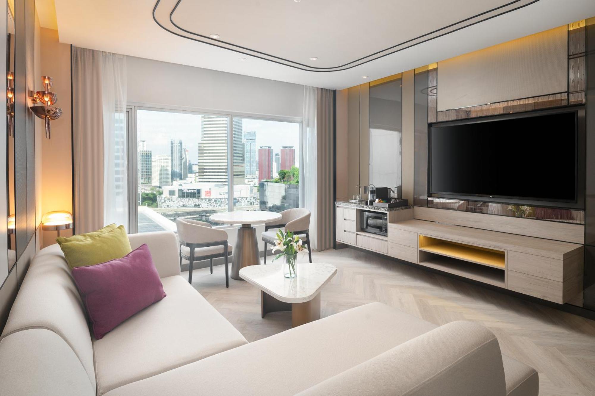 Pathumwan Princess Hotel - Sha Extra Plus Certified Banguecoque Exterior foto The photo shows a modern and stylish hotel room or living area. There's a light-colored sofa with decorative pillows in shades of purple and beige. In front of the sofa, there's a small coffee table. To one side, there is a dining table with chairs, 