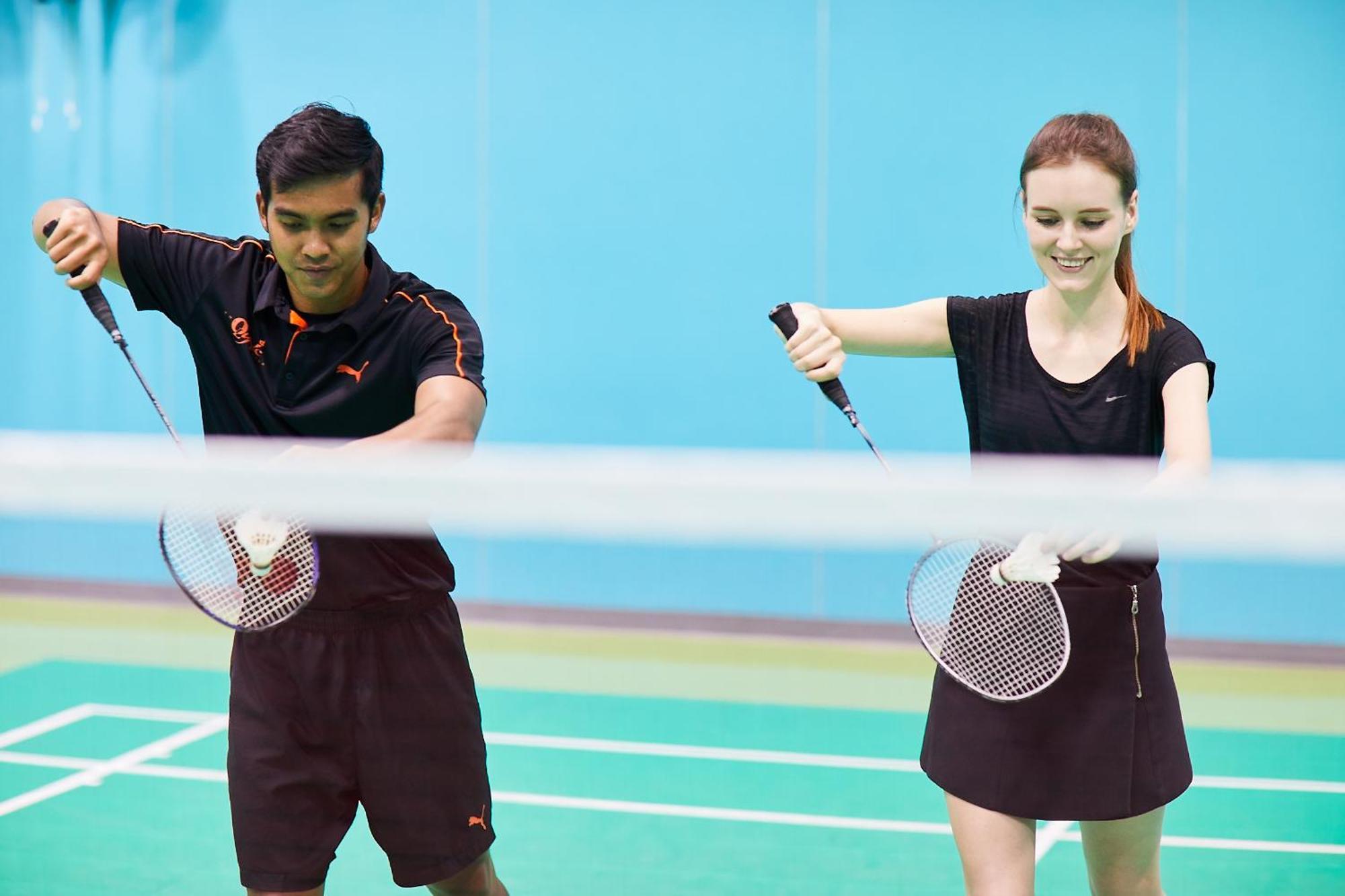 Pathumwan Princess Hotel - Sha Extra Plus Certified Banguecoque Exterior foto The photo shows two individuals engaged in a badminton practice session. They are on a court, with a net in the foreground. One individual, a male, is wearing a dark shirt with orange accents and shorts, while the other individual, a female, is dress