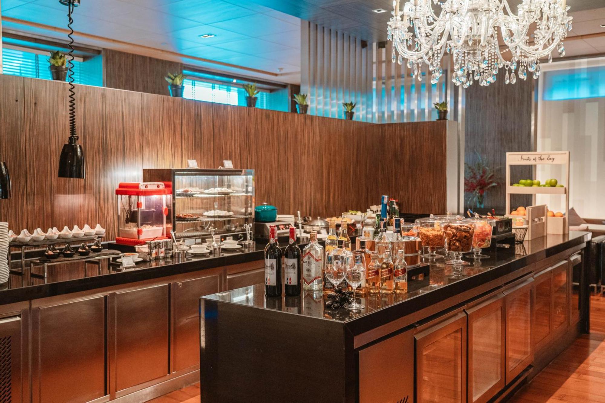 Pathumwan Princess Hotel - Sha Extra Plus Certified Banguecoque Exterior foto The photo depicts a stylish bar or buffet area within a restaurant or hotel setting. It features a sleek wooden backdrop with a modern design. The countertop is adorned with various drinks, including bottles of wine and spirits, arranged elegantly. T