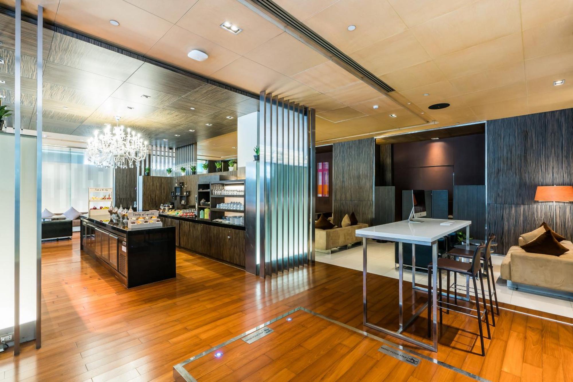 Pathumwan Princess Hotel - Sha Extra Plus Certified Banguecoque Quarto foto The photo shows a modern and stylish interior space, likely a lobby or lounge area. It features elegant wooden flooring and contemporary furnishings. On one side, there is a sleek, dark-colored counter or bar area with various items displayed, possib