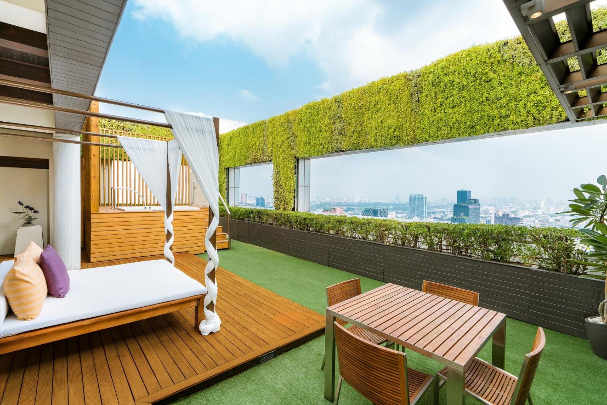 Pathumwan Princess Hotel - Sha Extra Plus Certified Banguecoque Quarto foto The photo displays a modern rooftop terrace with a lush, green wall and panoramic views of a city skyline. The area features a wooden deck with a white, draped lounging bed, creating a relaxing space. In addition, there’s a small dining table with se