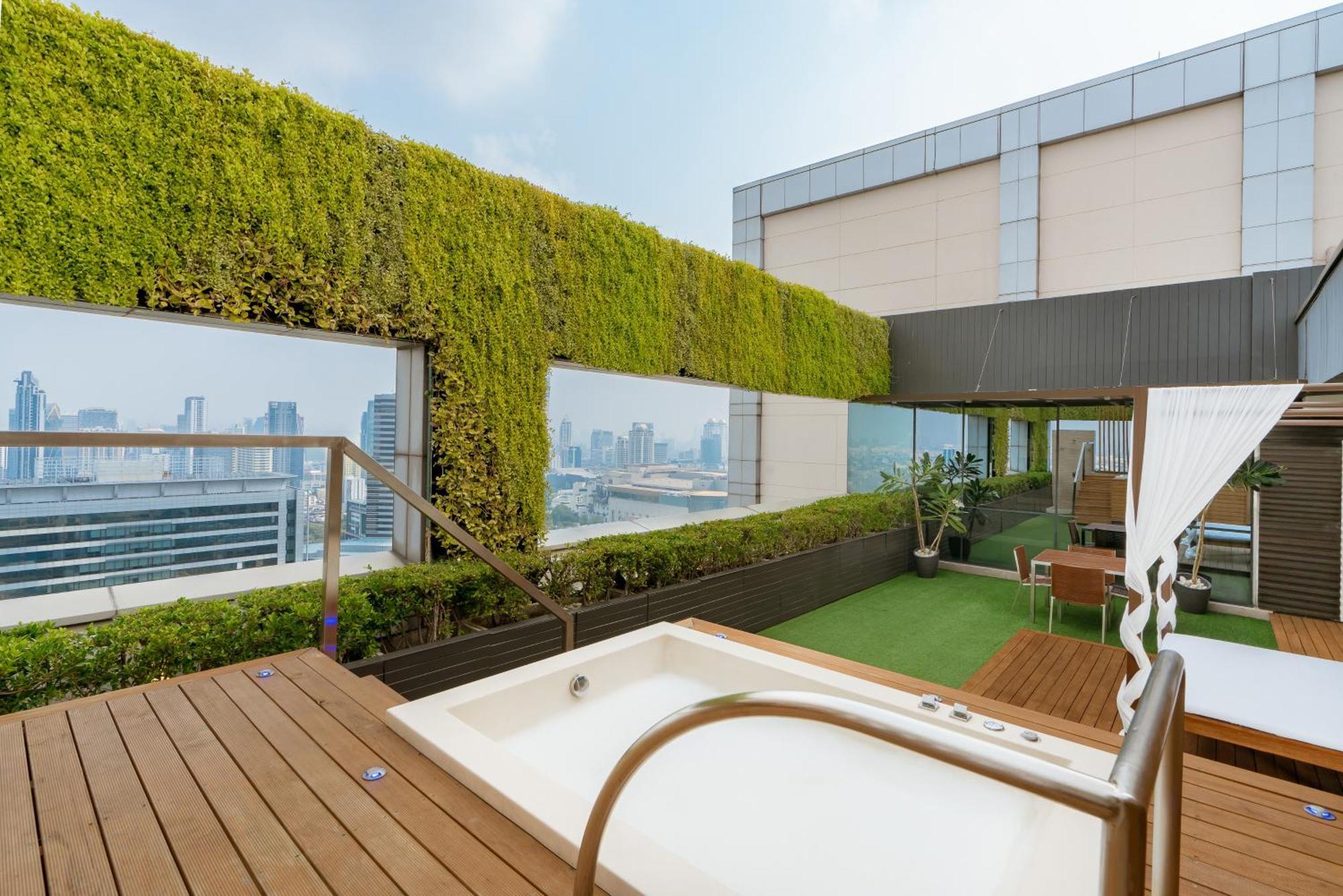 Pathumwan Princess Hotel - Sha Extra Plus Certified Banguecoque Quarto foto The photo shows a rooftop terrace featuring modern design elements. There is a small, white hot tub positioned on a wooden deck, and surrounding it are green plants and a lush vertical garden that adds a touch of nature. The area is elegantly furnish