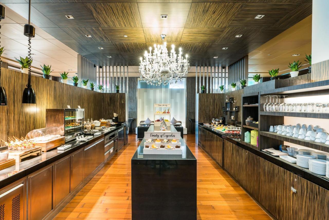 Pathumwan Princess Hotel - Sha Extra Plus Certified Banguecoque Exterior foto The photo shows a modern restaurant or buffet area with a stylish interior. The space features wooden walls and flooring, creating a warm ambiance. A large chandelier hangs from the ceiling, adding elegance to the setting. On the right side, there ar