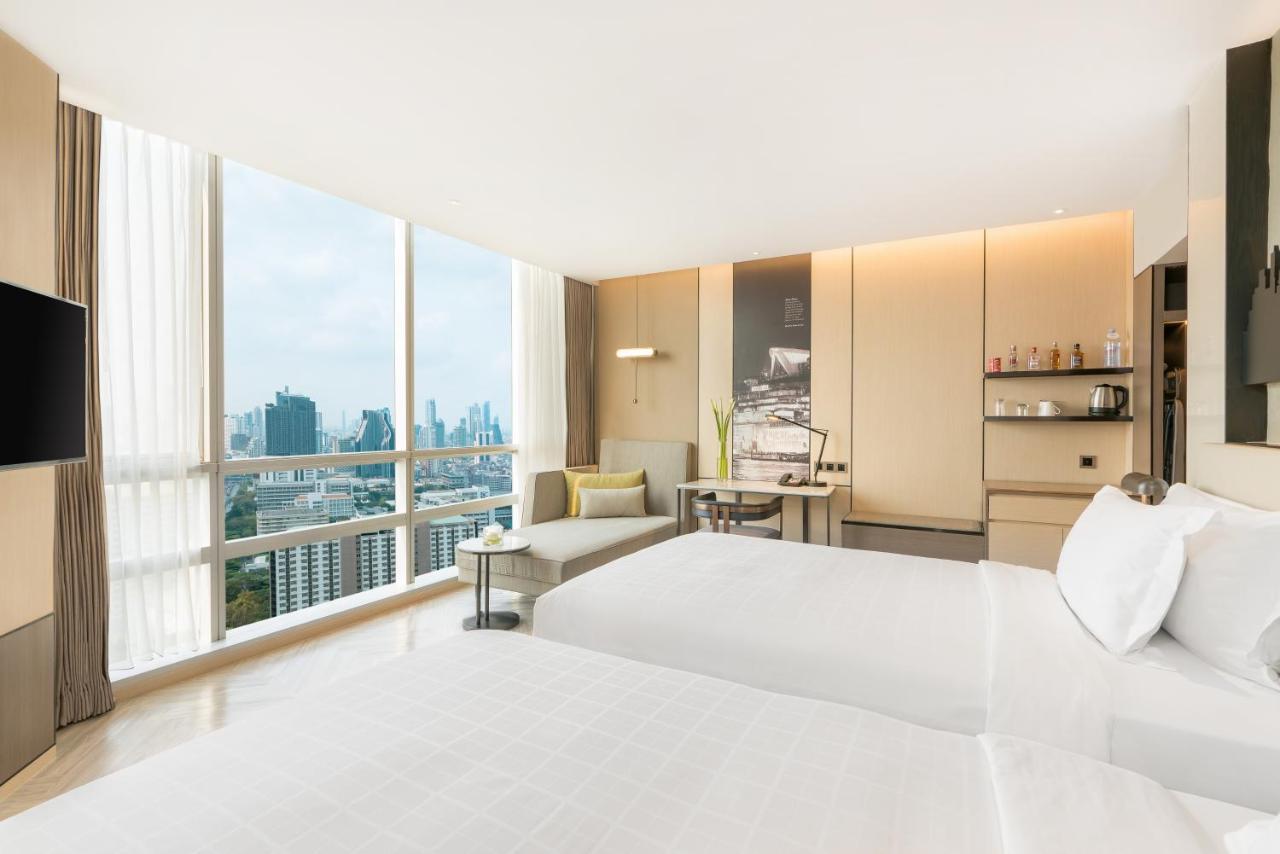 Pathumwan Princess Hotel - Sha Extra Plus Certified Banguecoque Exterior foto The photo shows a modern hotel room featuring two beds neatly made with white linens. Large windows allow natural light to flood the space, offering a panoramic view of the city skyline outside. The room is decorated in a contemporary style, with lig