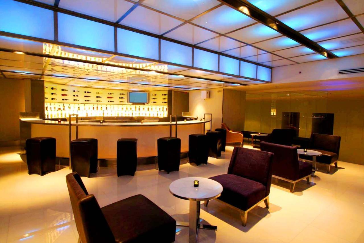 Pathumwan Princess Hotel - Sha Extra Plus Certified Banguecoque Exterior foto The photo shows a stylish and modern lounge or bar area. It features a contemporary bar design with a backlit display of bottles. The seating arrangement includes black and purple upholstered chairs and stools arranged around small tables. The lighti