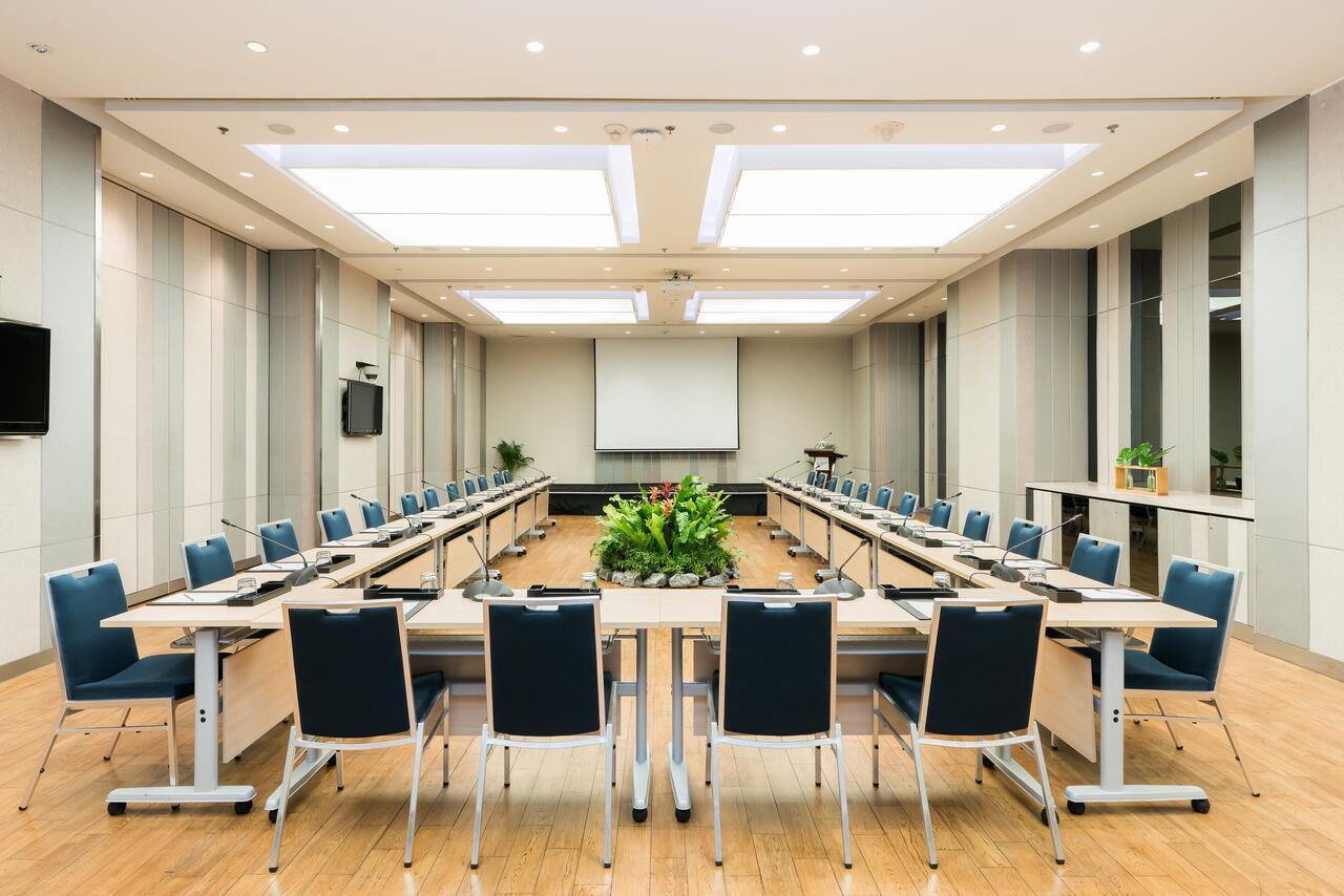Pathumwan Princess Hotel - Sha Extra Plus Certified Banguecoque Exterior foto The photo shows a modern conference room set up for a meeting. The room features a long arrangement of tables with chairs on either side, creating a U-shape. In the center, there is a small planter with greenery. The walls are neutral-toned, and ther